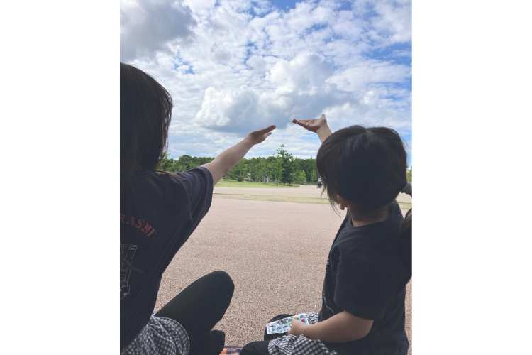 遠近法でひとつの雲を手に乗せる2人の子どもの後ろ姿